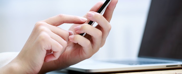 En närbild på en kvinnans hand, en mobiltelefon och en dator.