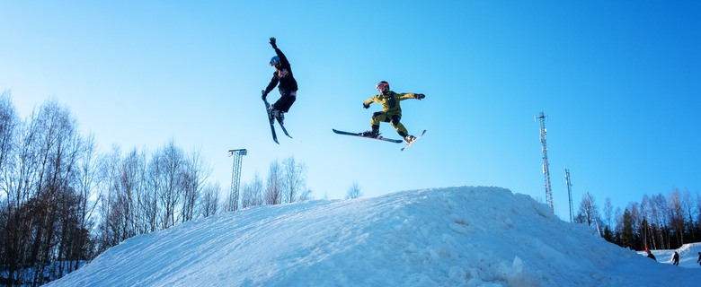 Två barn hoppar med skidorna i en uppbyggd kulle i Valbacken, Ingatorp.