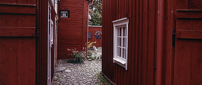 Fotografi där vi ser in genom porten till Fornminnesgården. Plank och byggnader är målade med rödfärg.