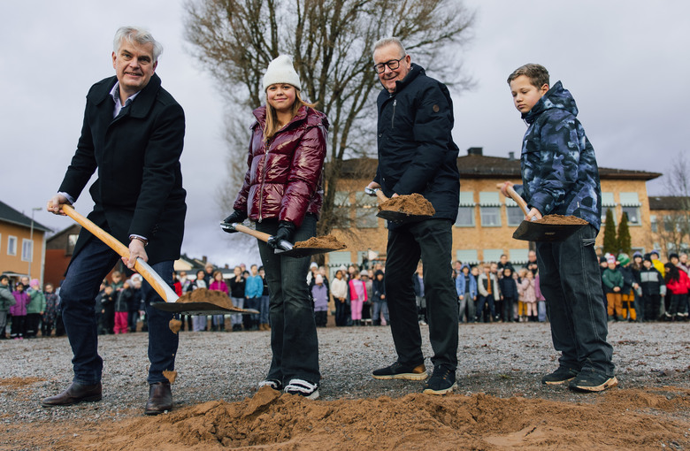 Två vuxna och två barn gräver upp jord med spade på skolgård.