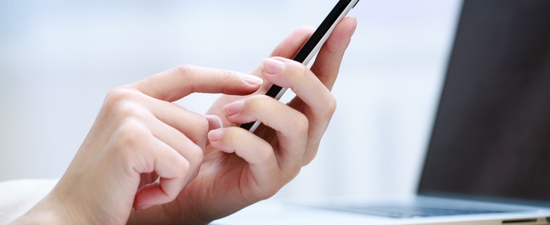 En närbild på en kvinnans hand, en mobiltelefon och en dator.