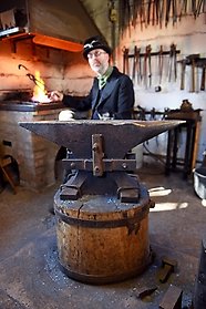 Fotografi av smeden i sin smedja, bakom ässjan