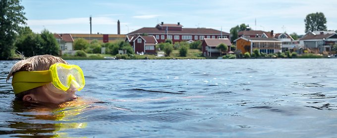 Barn med cyklop badar i sjö.