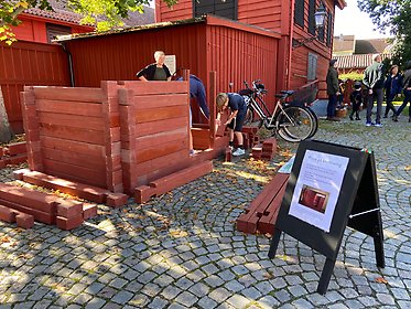 En familj provar på knuttimring med museets trähusmodell på Museigården