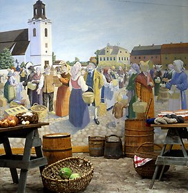 Foto över torget i den stadshistoriska utställningen, i fondmålningen pågår torghandel, på kullerstensgolvet står en vagn, korgar och olika sorters ämbar med varor.