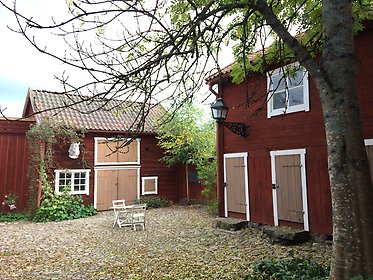 Stadsgård med röda timmerhus runt en kullerstensbelagd innergård.